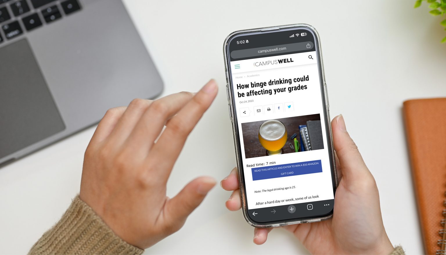 student reading CampusWell on phone at desk | wellness on college campuses